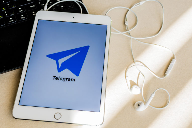 Telegram app on tablet next to earbuds and laptop