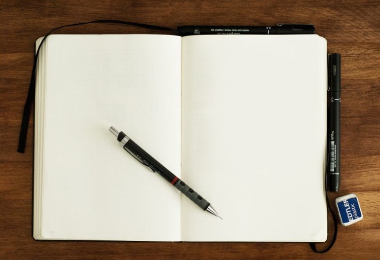 A pen sits on an open notebook on a wooden table.