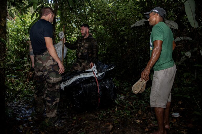 Lieutenant Colonel Bataillon, the gendarmerie's mission leader, finds this black trash bag in the forest, where illegal gold miners have stashed their mining equipment to hide it from the gendarmes. The miner on the right comes back out of hiding to negotiate with Bataillon what he can keep and what not. Usually, the gendarmes leave clothes and personal items and anything used for mining is burned. Image by Gerno Odang/DIE ZEIT.