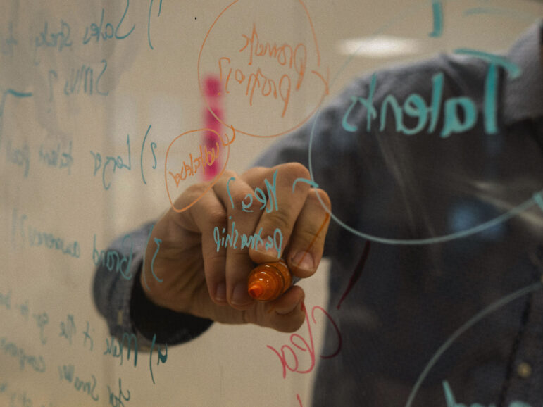 A person draws project plans on a see-through meeting room wall in coloured pen.